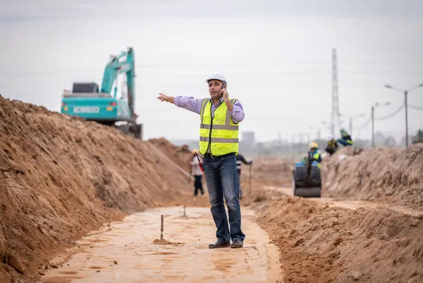 Supervisor en obra con casco y chaleco, hablando por teléfono ejemplifica ¿Por qué la seguridad industrial es vital en una obra?