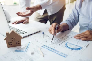 Ingenieros revisan planos arquitectónicos con maqueta de casa. Esencial para la gestión de proyectos inmobiliarios