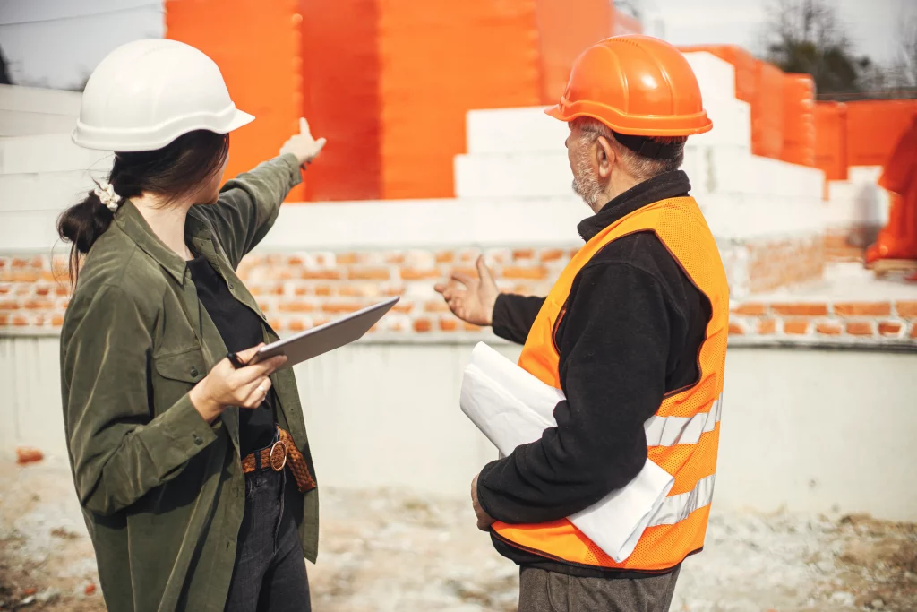 Supervisores con cascos discuten detalles de obra con planos y tablet, para la evaluación de riesgos para construcción