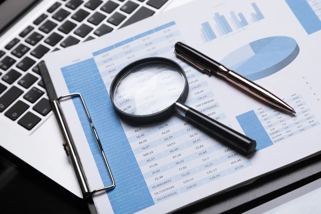 Lupa y pluma sobre un informe de datos y gráficos. Herramientas de análisis para la auditoría de cumplimiento normativo STPS