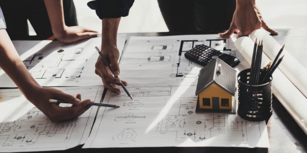 Manos señalando planos técnicos con maqueta de casa representando empresas desarrolladoras de proyectos inmobiliarios.